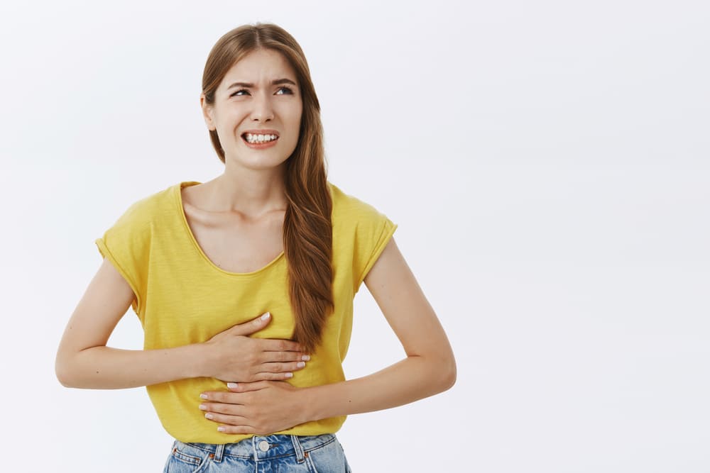 Menina com mãos no abdômen com expressão de dor