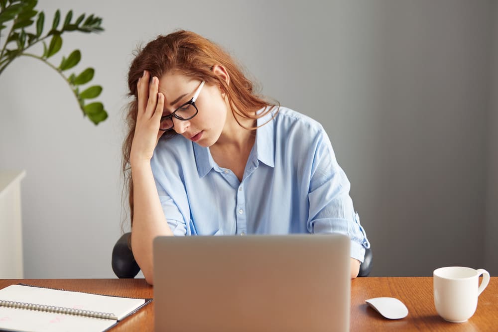Mulher sentada em frente ao notebook com expressão de estresse