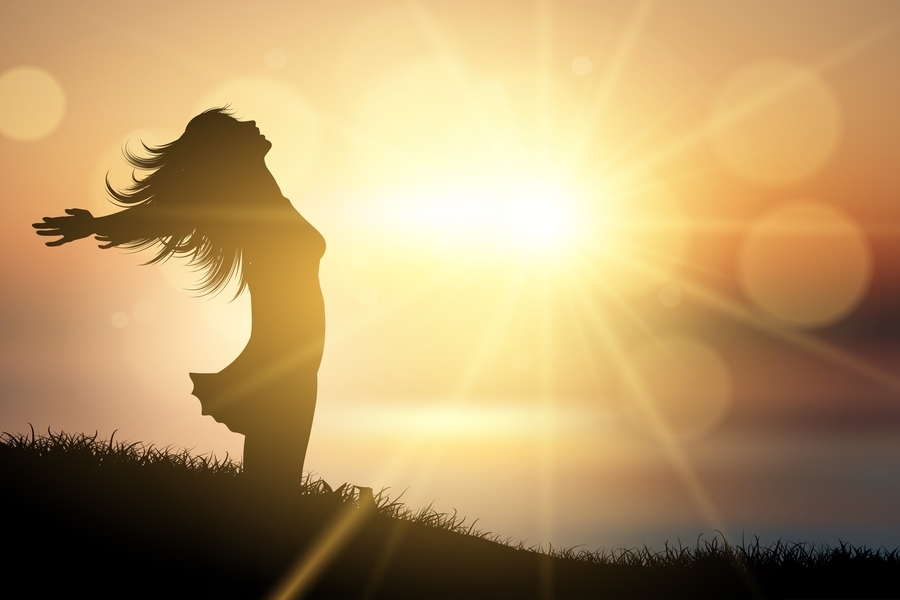 Mulher com braços abertos em frente ao sol